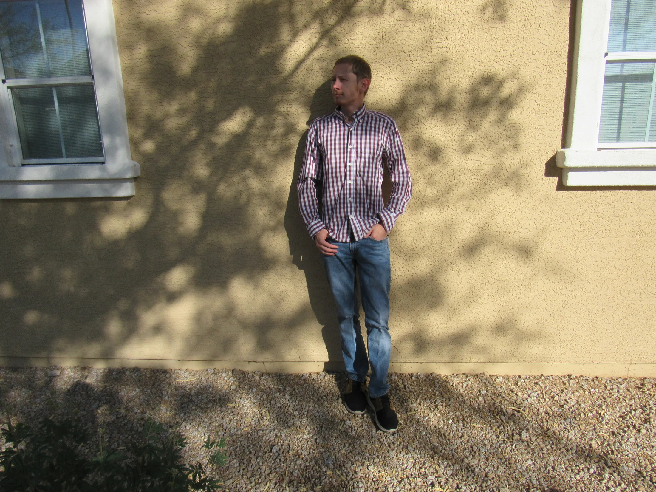 Portrait of Ryan against a stucco wall crossed by tree shadows