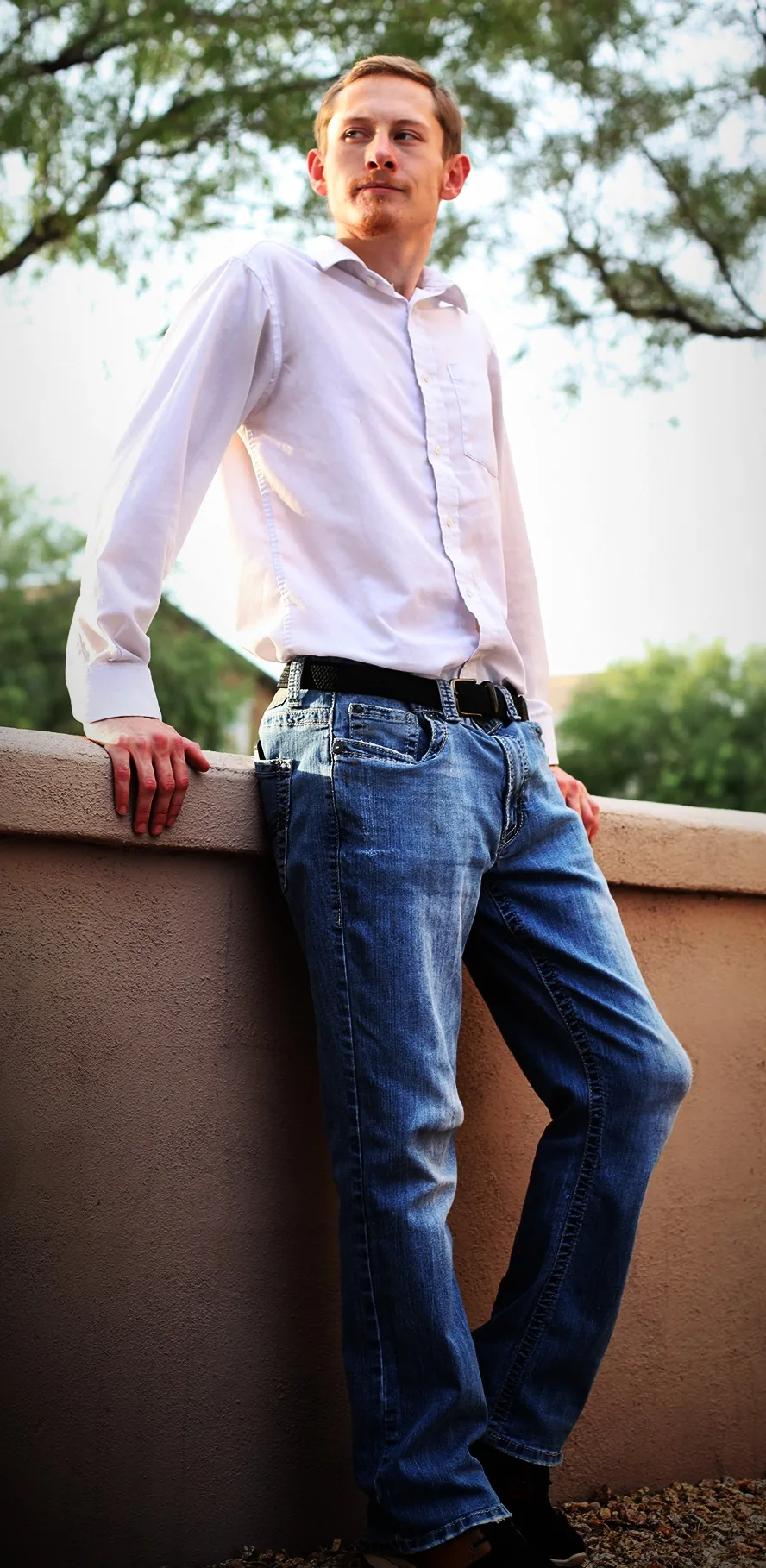 Ryan leaning against a low outdoor wall in a vertical portrait