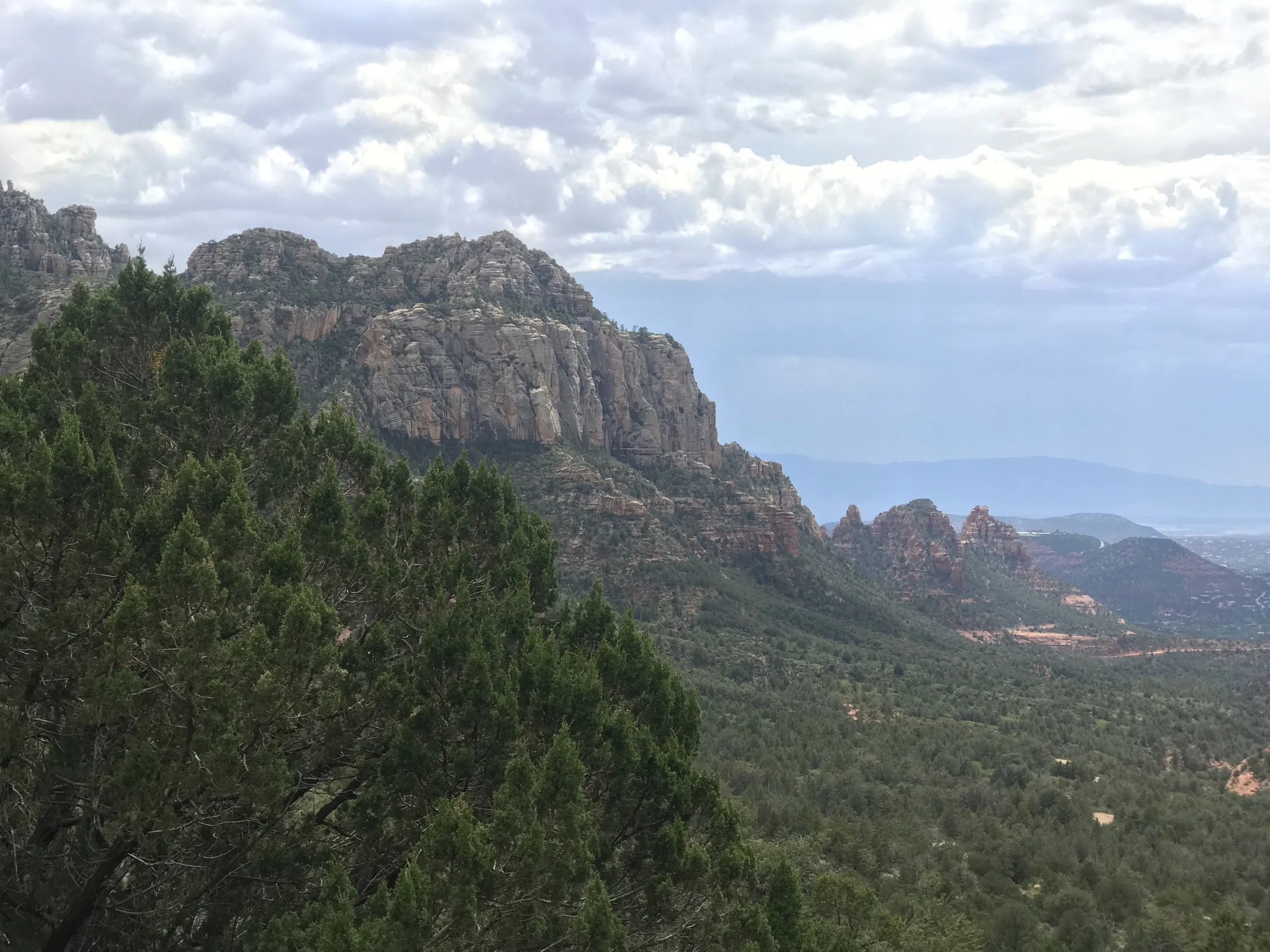 Sedona cliff and forest beneath bright broken clouds